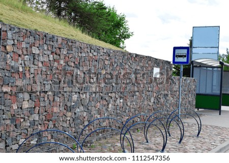 Bus stop with blank white billboard and blue traffic sign on  decorative rock wall background.
