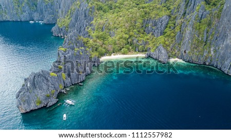 Aerial drone view of boats above a tropical coral reef and small sandy beach surrounded by huge cliffs (Secret Lagoon, Miniloc) Royalty-Free Stock Photo #1112557982