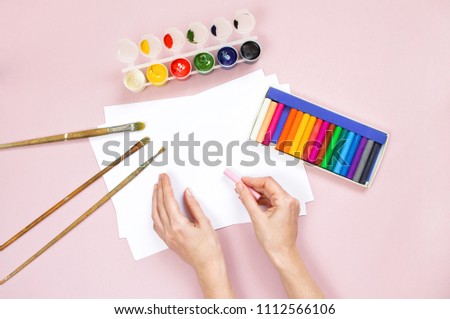 Artist home office desk workspace women's hands Paper watercolors paint brush on a pink background. Flat lay, top view creative minimal mock up template.