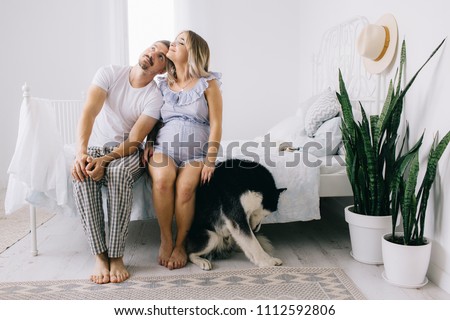 Pregnant woman, man and dog lying on a bed in the bedroom, playing games and walking