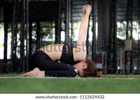 Woman in dark sportswear practicing yoga on lawn