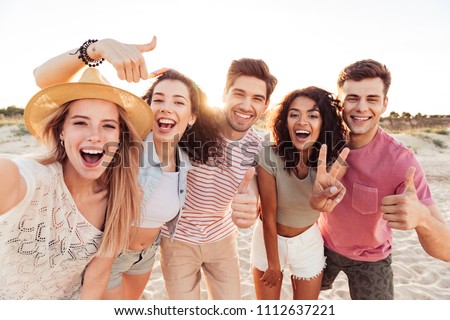 Group of happy young friends in summer clothes taking a selfie while standing at the beach