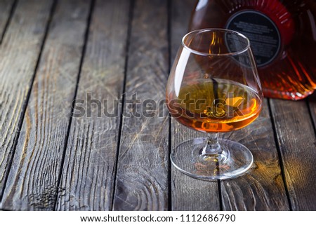 Glasse of brandy or cognac and bottle on dark background.