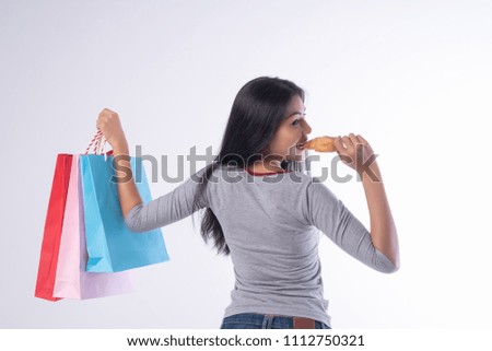 Happy Asian girl eating bread with shopping bags in hand on white background