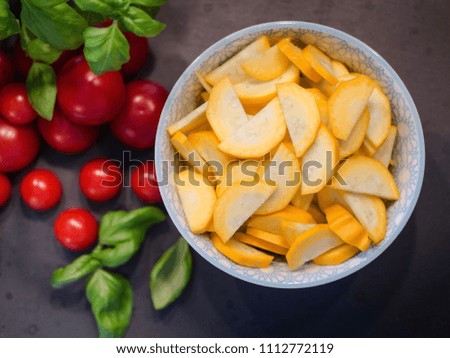 Slices of yellow zucchini in bowl on the right side of the picture. Tomatoes on the left in the background. Top view and black background.  Italian food.