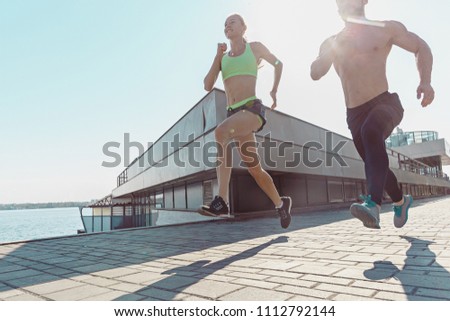Pretty sporty woman and man jogging at city at morning. Fit fitness young caucasian girl and boy running. Female sports models in summer sunny day exercising outdoor