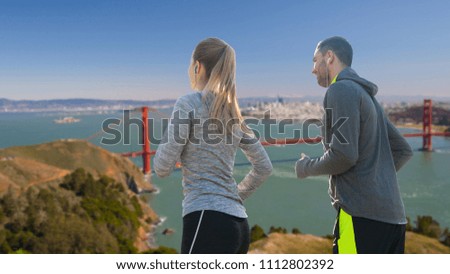 fitness, sport and technology concept - happy couple running and listening to music in earphones over golden gate bridge in san francisco bay background