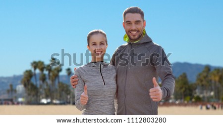 fitness, sport and gesture concept - smiling couple outdoors showing thumbs up over venice beach background in california