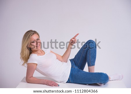 portrait of a beautiful blonde girl on a white background lying on a table. She lies directly in front of the camera smiling and looking happy