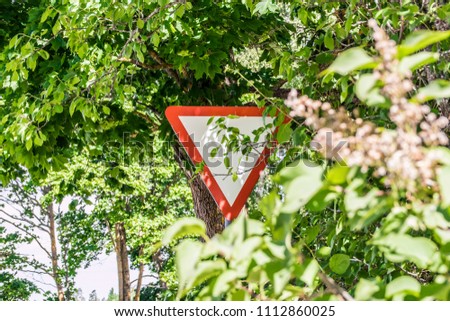 Dangerous traffic situation, overgrown bush leaves tree branches covering give way yield sign. Traffic hazard concept. Can not see the sign from the road.