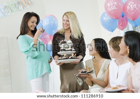 Pregnant woman taking picture of friends having cupcake at a baby shower