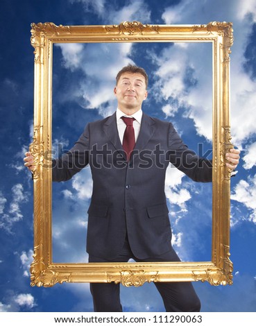 Portrait of businessman holding a golden frame on blue sky with clouds