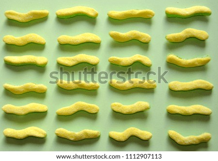 Rows of yellow sour worm candy on pastel green background