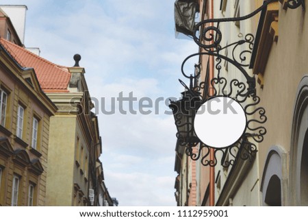 Blank round signboard, hanging from wrought iron bracket in the city, classic architecture buildings background.