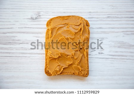 Single toast with peanut butter over white wooden background, top view.