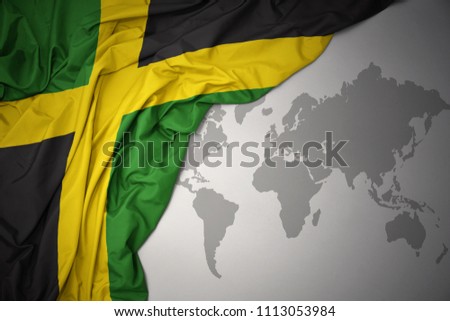 waving colorful national flag of jamaica on a gray world map background.