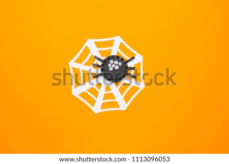 Holiday decor on Halloween. A spider made of black paper with white eyes on an orange background. The child did the work. View from above. Flat lay
