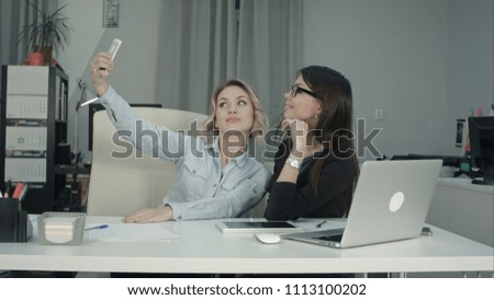 Two female colleagues taking selfie with phone in the office