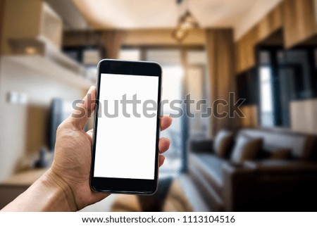 A man hand holding smart phone device in the bright office room interior.