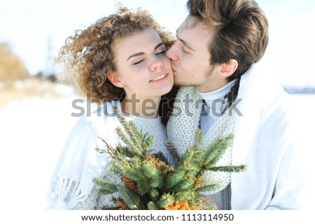 Man hugging woman keeping fir tree branches in white winter background. Concept of romantic photo session.