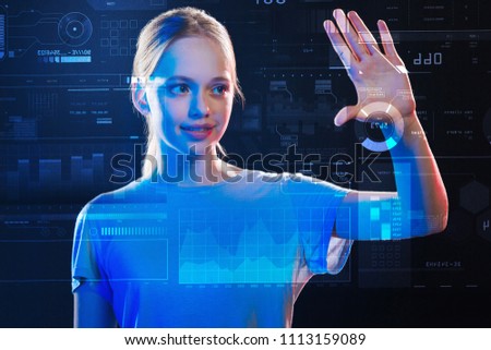Cheerful teenager. Clever schoolgirl feeling interested and smiling while being at the lesson of computer studies and touching the icon on a transparent screen