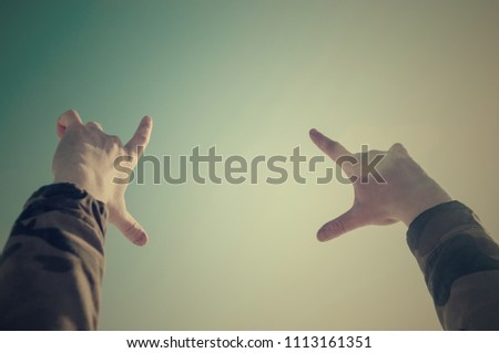Hands of a man in camouflage showing a square against the background of the icy lake with horizon.