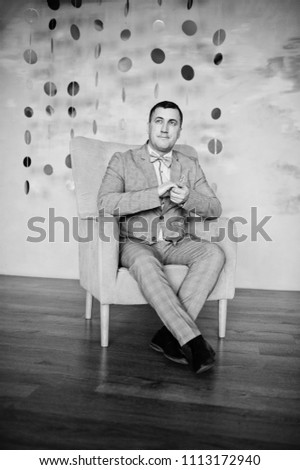 Studio portrait of man in suit near chair.