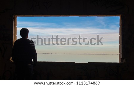 Person looking through the window at the landscape. It is the Mar Menor. In the background you can see La Manga