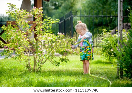 Barefoot cute girl watering the plants and flowers from hose spray. Gardening in the backyard. Caring for her plants in spring and summer