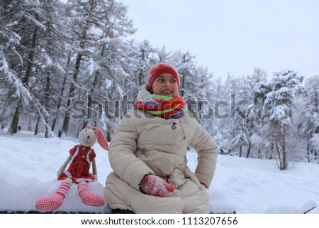 A girl is walking with a toy rabbit in a snowy forest