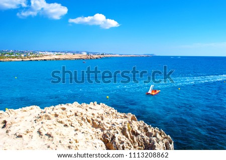 Image of calm sea surface near Agia Napa, Cyprus. One orange paddleboat in deep blue water against rocky coast and cape Greco on the background. Warm day in fall. Concept of leisure and recreation