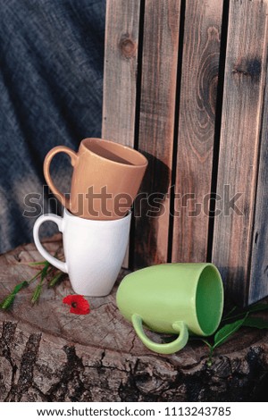 New mugs on a wooden stump, with a red flower, on a background of gray fabric and a wooden box. Still life. Photo of dishes