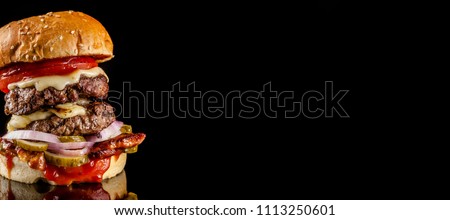 The concept of American fast food. Juicy American burger with two beef cutlets, with sauce and ogretsami on a black background. Copy space