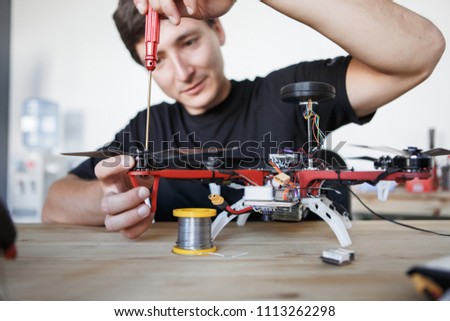 Picture of man with screwdriver fixing square copter at table