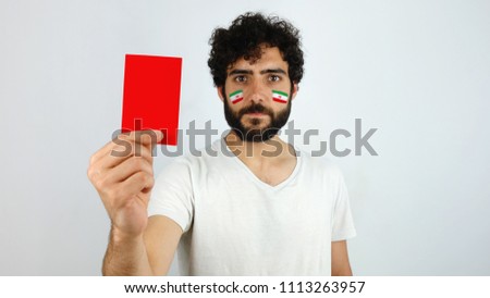 Sport fan holding a red card. Man with the flag of Iran makeup on his face and white t-shirt         
