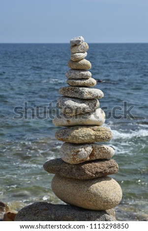 Tower of zen stones on rocky coast with sea and horizon in background. Vertical view.
