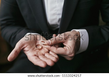 Wedding rings on palm hand. Groom in stylish suit holding golden wedding rings in hands, sitting in the room. marriage or divorce concept