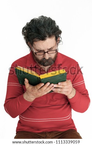 a curly haired, gray haired, bearded man with  glasses and a red sweater is reading a book. Isolated on white background