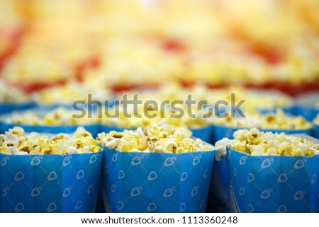 Blue package with popcorn. It can be seen that there are also a lot of popcorn in the background, in anticipation of a good movie in the cinema.