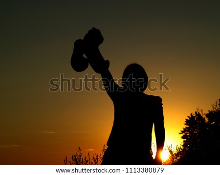 A girl with boxing gloves in the hand. Silhouettes of a boxer woman with a raised hand up. Sunset. Sportswoman holding boxing gloves in the box. Winner