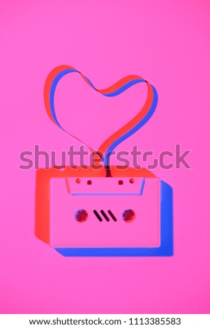 toned pink picture of retro audio cassette with tape in heart shape on tabletop