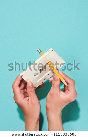 partial view of woman holding white retro audio cassette and pencil isolated on blue