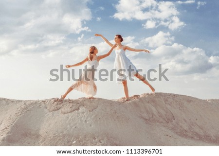 Two beautiful dancers make dance steps on the sand in the desert.