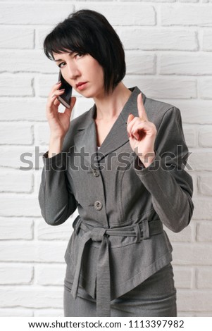 business woman dressed in a gray suit talking on the phone, stay in front of a white wall