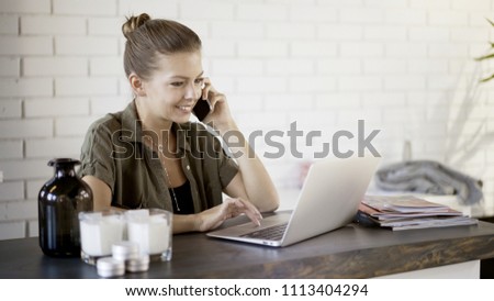 A young happy smiling busy blond casual pretty woman freelancer businesswoman is working at home with a laptop having a call background of a white brick wall