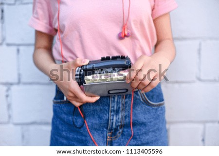 cropped shot of woman with earphones holding retro cassette player in hands against white brick wall