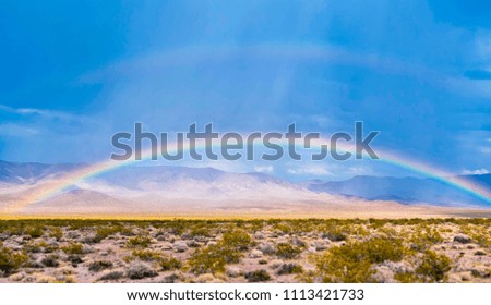 Beautiful rainbow over an American desert with hills and mountains in the background and a clear blue sky for copyspace