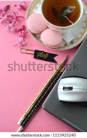 Top view of pink hyacinth, laptop, tea cup, cell phone and French macarons on pink background. Feminine workspace desktop with copy space.