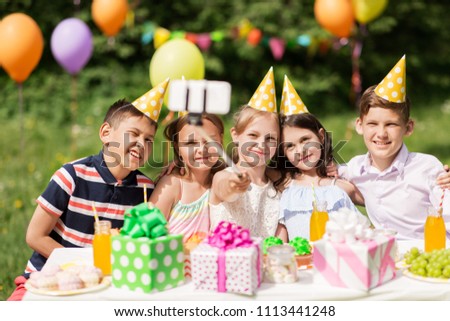 holidays, childhood and technology concept - happy kids taking picture by selfie stick on birthday party at summer garden