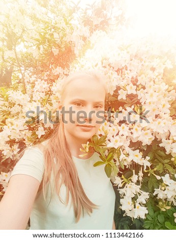 Beautiful teenager blonde girl make selfie on blooming spring rhododendron trees background. Mobile shot.